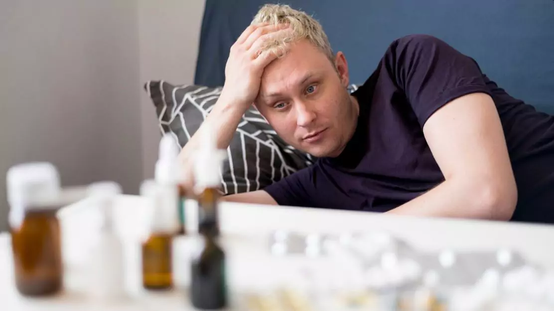 Man lying on bed with a stressed expression, looking at various prescription bottles and pills, representing the use of depression medication near Hall Lake