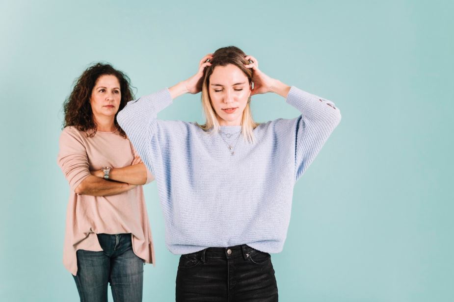 A girl with bipolar disorder showing distress while her mother stands with arms crossed, seeking support from United Healthcare Psychiatrist near Hwy 90a Commercial Park in a calming environment.
