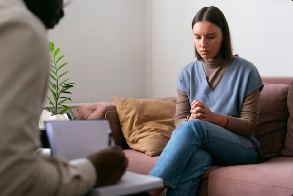 A woman sits on a couch looking pensive during a therapy session, representing the need for Depression Medication in Fluor Central