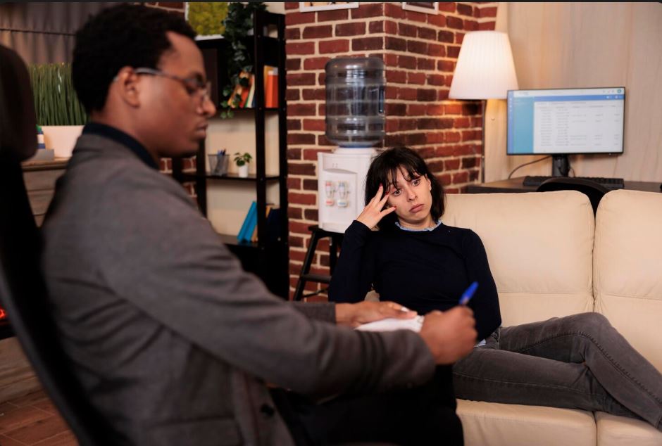 A patient consulting with an Anthem Insurance Psychiatrist in Hwy 90a Commercial Park, taking notes in a cozy office with a brick wall and water cooler