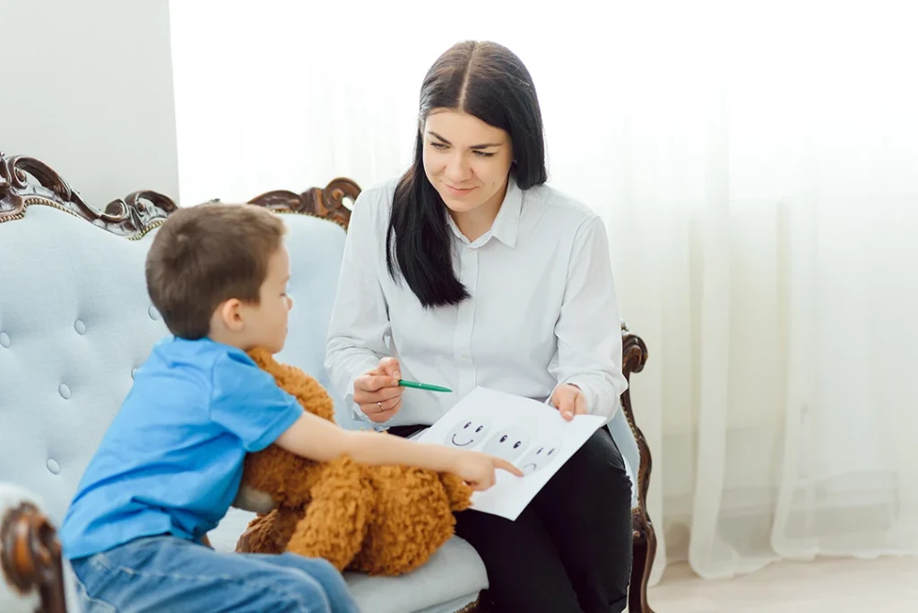 Therapist noting observations while conversing with boy hugging teddy bear on couch, illustrating compassionate same-day ADHD testing in Sugar Land for efficient child assessments.