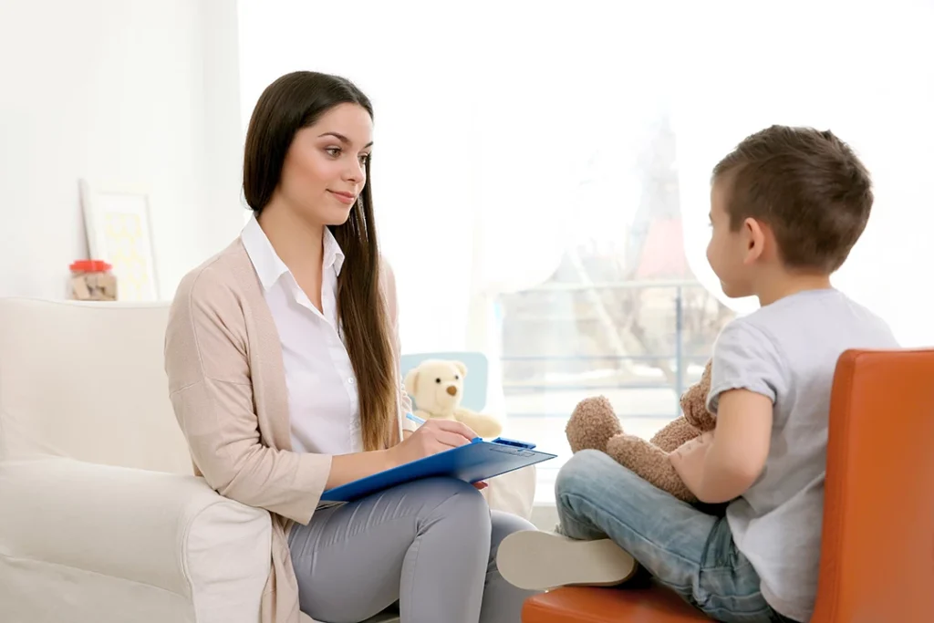 Therapist noting observations while conversing with boy hugging teddy bear on couch, illustrating compassionate same-day ADHD testing in Sugar Land for efficient child assessments.