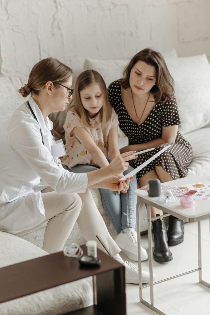 Doctor explaining bipolar treatment options to child and parent in Sugar Land, pointing to informational sheet during family therapy session in cozy clinic.