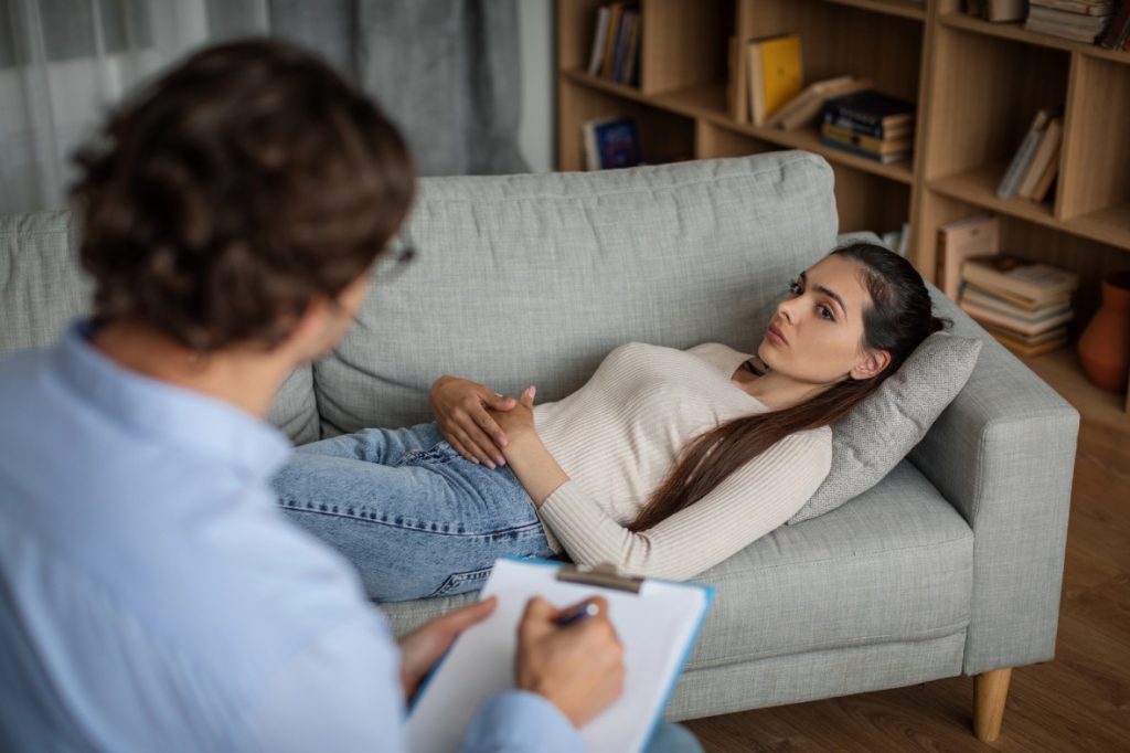 Adolescent Depression Psychiatrist Sugar Land therapy: client on couch in cozy office speaking with therapist taking notes, mental health care