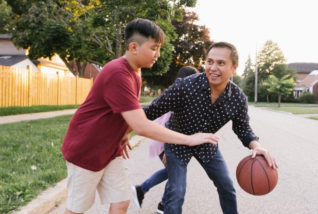 Father and son playing basketball on Sugar Land street, promoting parent support and adolescent depression help resources.