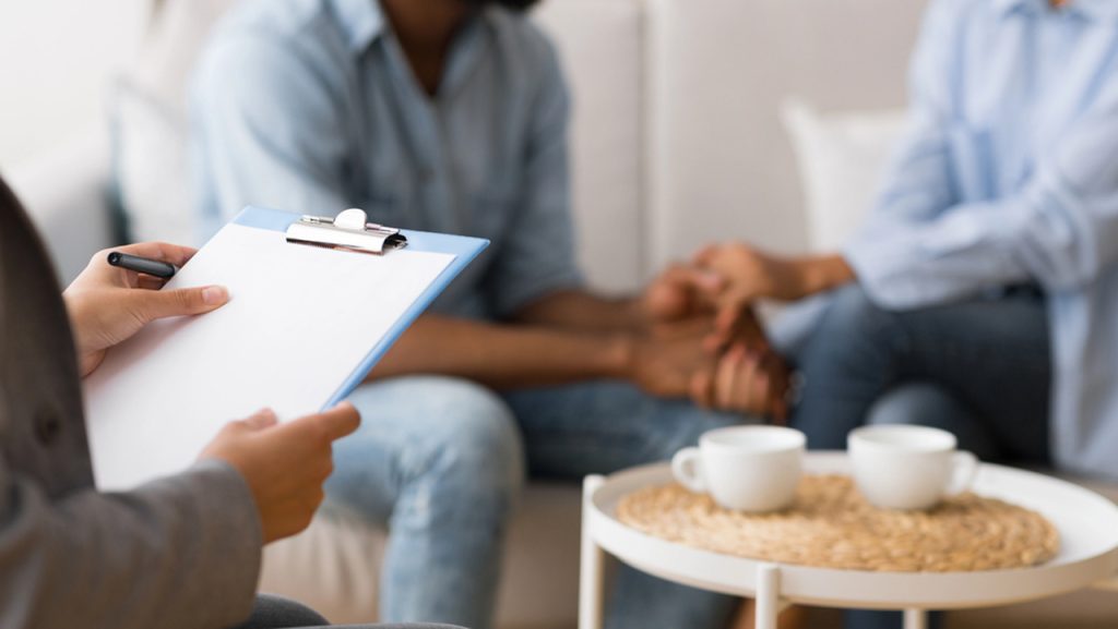 Therapist holding clipboard during supportive couples therapy session, representing compassionate mental health care with Cigna Insurance Psychiatrist Sugar Land.