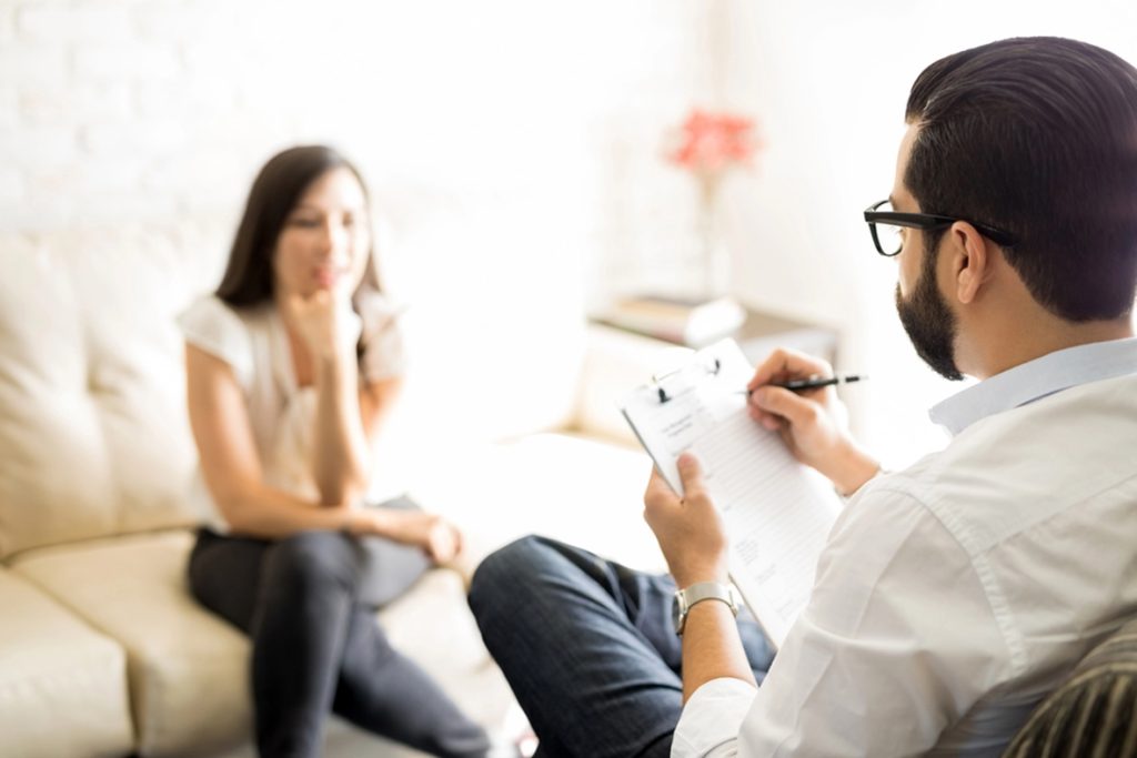 A woman sitting on a couch while speaking with a therapist who is taking notes, representing challenges with focus and attention in ADHD with ADHD Doctor Sugar Land.