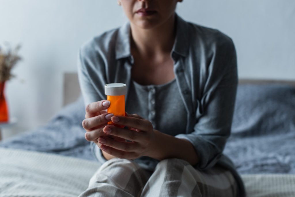 A woman sits on her bed holding a bottle of prescribed depression medication Sugar Land, contemplating her mental health treatment.