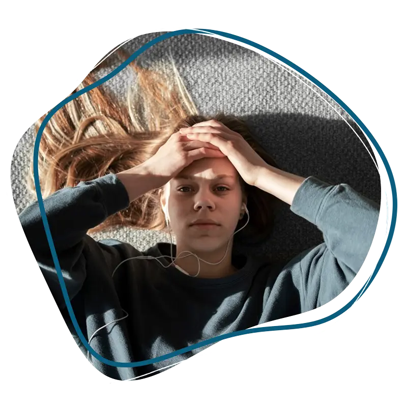 A woman lying on a carpeted floor looking stressed while wearing earphones, used to represent mental health support from a bipolar psychiatrist accepting insurance.