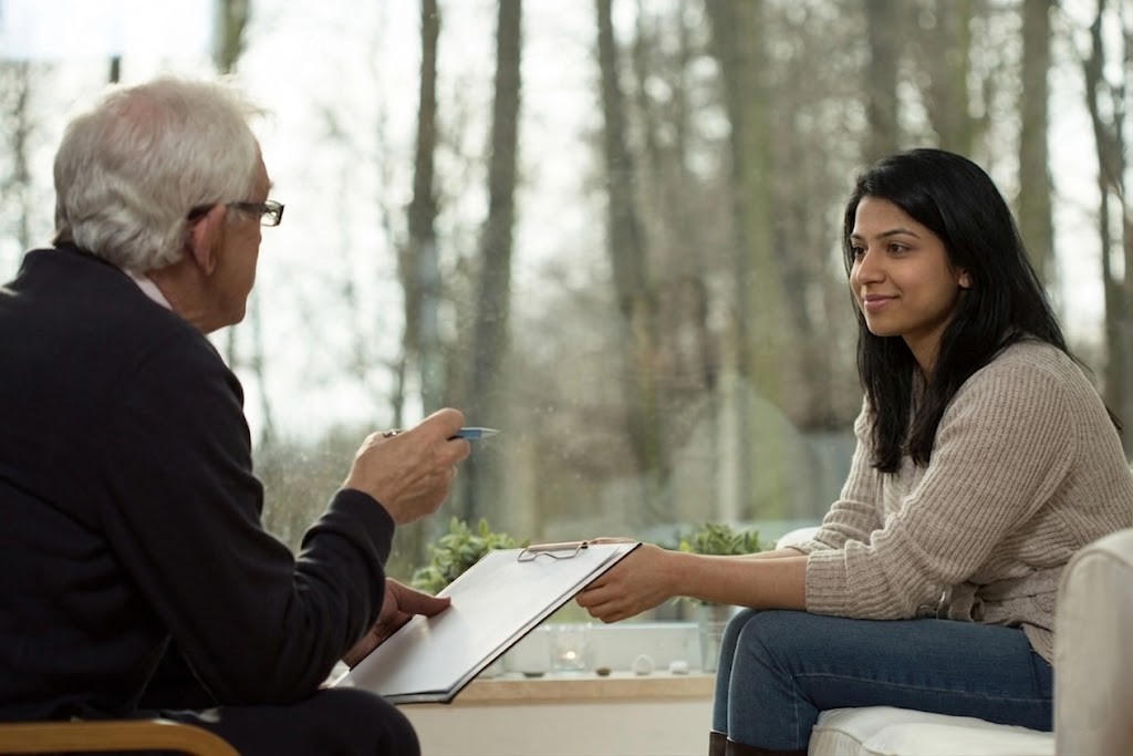 Friendly young patient in beige sweater meets with her anxiety doctor in Sugar Land, overlooking a garden.